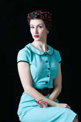 An attractive young woman dressed up in 60’s wear against a grey studio background. Portrait of a beautiful model looking at the camera dressed in a retro style