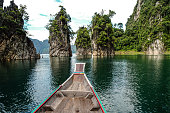 Wooden Thai traditional long tail boat on a lake with limestone mountains in Khao Sok National Park, Surat Thani Province, Thailand. Beautiful landscape.