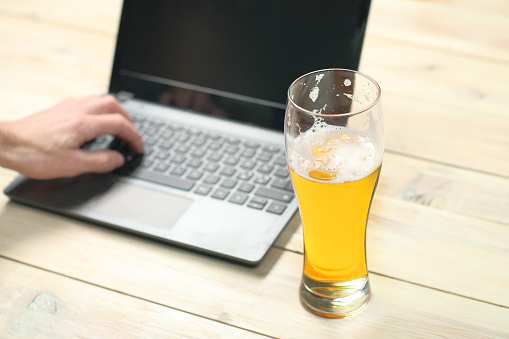 mug with beer on the background of hands and a laptop on a wooden table