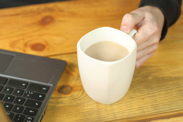 istock person holding a mug with coffee next to a laptop 1459152898