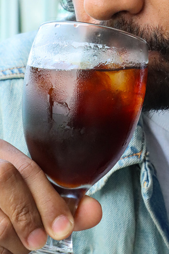 Stock photo showing a close-up view of a wineglass of iced coffee being drunk by an Indian man as part of an al fresco breakfast brunch.