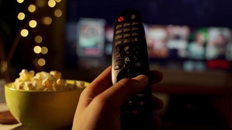 A human hand holding remote control with a bowl of popcorn