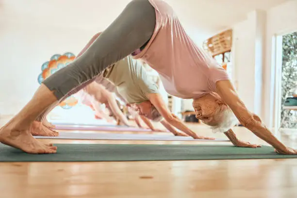Photo of Yoga, exercise and senior woman in studio, class and lesson for wellness, body care and fitness. Sports, balance and elderly female doing downward dog pose for training, pilates and workout in gym