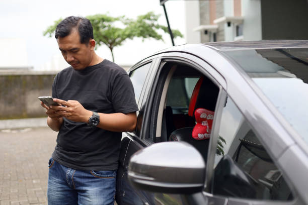 istock Asian online driver standing beside his car while holding a cell phone 1459155972