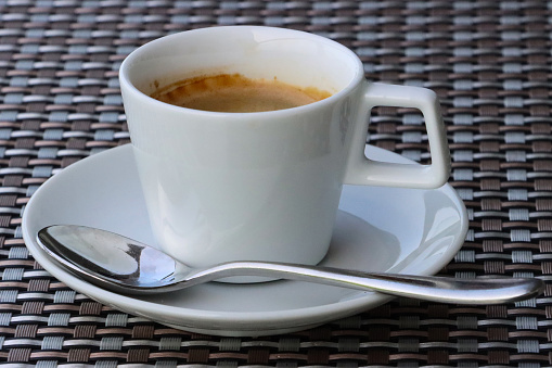 Stock photo showing a cup of black coffee complete with white saucer. The freshly brewed coffee is being served on a table at a cafe, a hot energising beverage ready to drink.