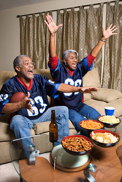 Couple watching sports on TV. Mature African-American couple cheering and watching football game at their home on television. old football stock pictures, royalty-free photos & images