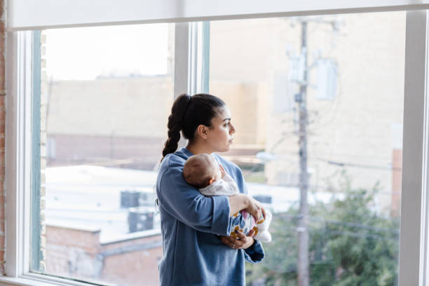 istock Sad young mom holds baby and looks out window 1459157294