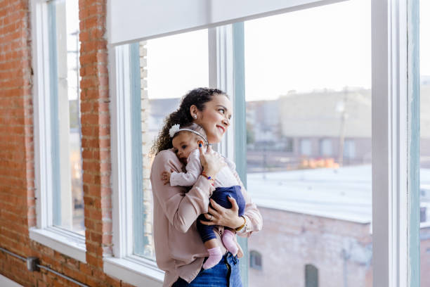 istock Cheerful young mom cuddles baby while looking out window 1459157312