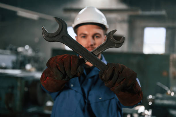 istock Holding two wrenches. Factory worker in blue uniform is indoors 1459159402