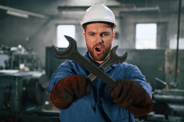 istock Holding two wrenches. Factory worker in blue uniform is indoors 1459159432