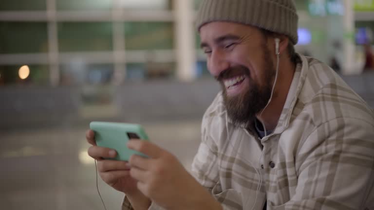 Smiling young man watching his cell at the bus station. Male in train Station, hanging out.