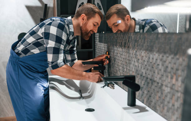 istock Side view. Fixing water tap. Plumber in blue uniform is at work in the bathroom 1459162533