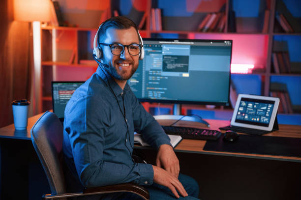 Positive professional programmer is working indoors and smiling. Neon lighting stock photo