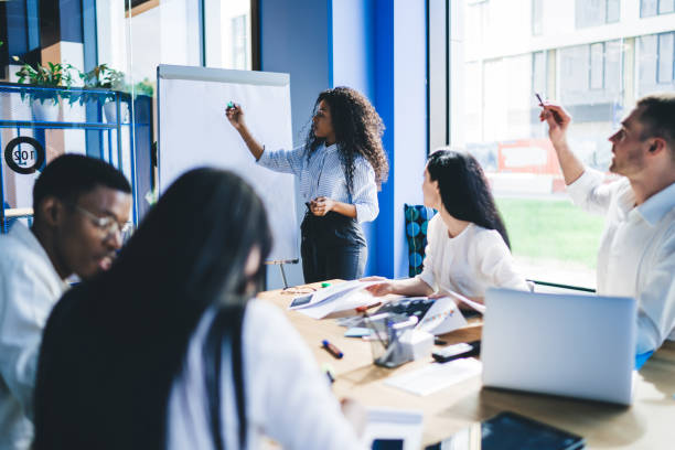 istock Manager writing notes on board with coworker in meeting room 1459168038