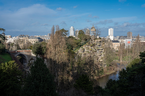 Park des Buttes Chaumont. View of the Footbridge joining the belvedere island, the Temple of the Sibyl and buildings behind