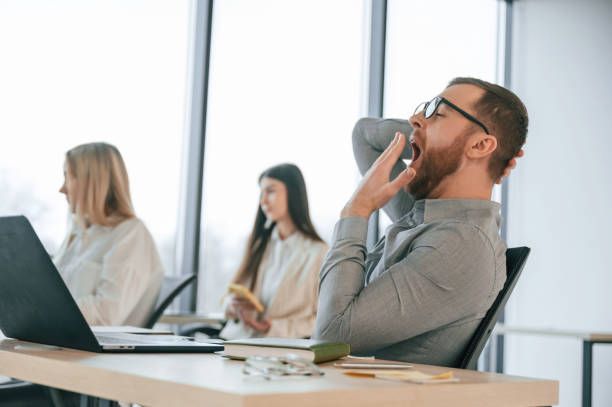 The man yawns, wants to sleep, tired. Successful team are working together in the office. Conception of business stock photo