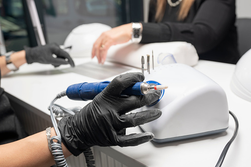 Manicurist is using a electric nail file drill in beauty salon. Young woman getting a manicure. Beautiful hands and nails. Macro photo. Nail Care.