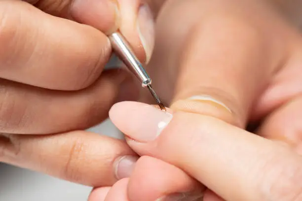 The manicurist is painting woman's fingernails with a thin brush in beauty salon.  Manicurist is using a brush in beauty salon. She is applying nail polish. Young woman getting a manicure. Beautiful hands and nails. Macro photo. Nail Care.