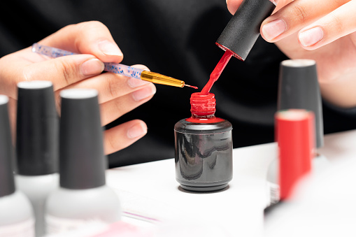 Nail polish drop, Nail polishes. The manicurist is painting woman's fingernails with a thin brush in beauty salon.  Manicurist is using a brush in beauty salon. She is applying nail polish. Young woman getting a manicure. Beautiful hands and nails. Macro photo. Nail Care.