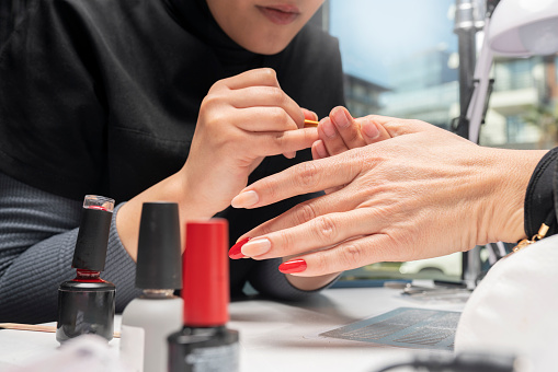 The manicurist is painting woman's fingernails with a thin brush in beauty salon.  Manicurist is using a brush in beauty salon. She is applying nail polish. Young woman getting a manicure. Beautiful hands and nails. Macro photo. Nail Care. Nail polish drop, Nail polishes.