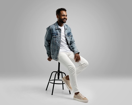 Handsome young african american guy sitting on stool, posing in studio - isolated.