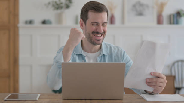 istock Happy Young Man Doing Paperwork on Laptop in Office 1459177982