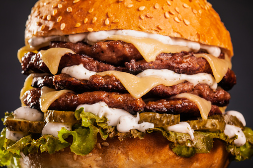 Abstract fast food. Quadruple burger with cheese cucumber and lettuce. Junk food against dark background.