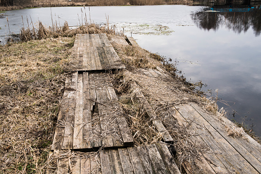 Old wooden bridge on the shore of the lake, on a cloudy day in sping, Belarus.