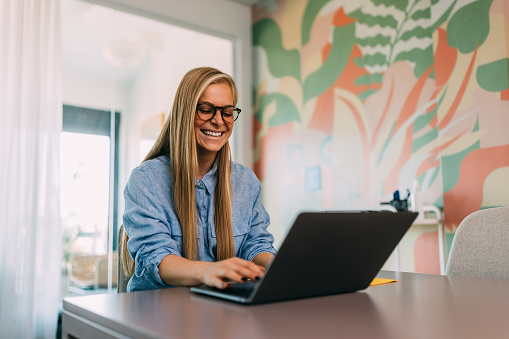 Smiling blonde girl working online, at the office, wearing glasses.