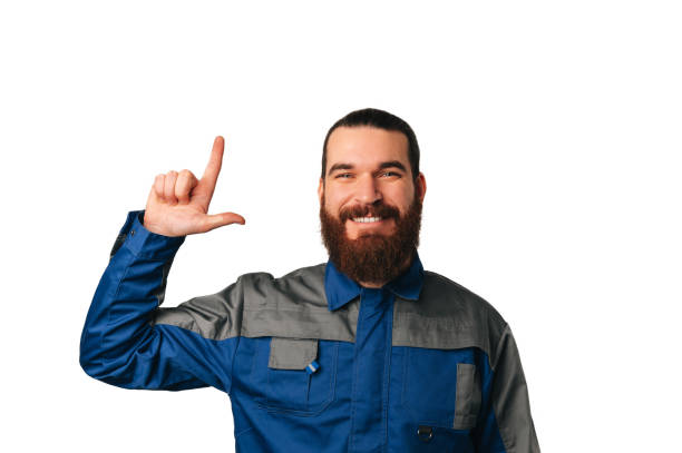 istock Smiling bearded male engineer wearing blue uniform points up to copy space. 1459182677
