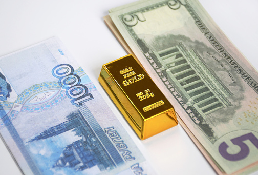a gold bar, Russian rubles and American dollars stacked in bundles on a white background. the struggle of the economy in the face of severe sanctions, inflation and economic crisis