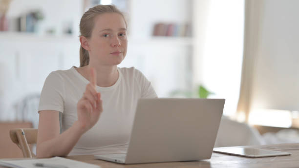 istock Rejecting Beautiful Young Woman Waving Finger in Denial while using Laptop 1459183985