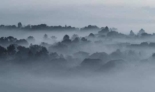 Village buildings houses and trees in low lying dense fog clouds moody morning haze in Gemeinlebarn in Lower Austria