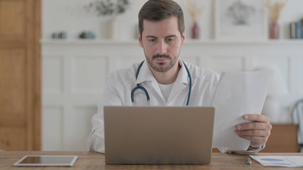 istock Young Doctor Doing Paperwork on Laptop in Clinic 1459189715