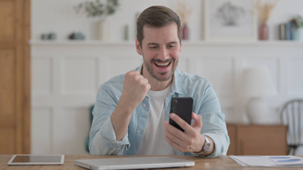 istock Successful Young Man Celebrating on Smartphone in Office 1459191427