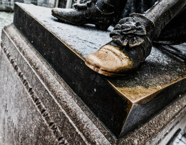 Cambridge, Massachusetts, USA - January 23, 2023: Close-up of the shoe toe of the John Harvard statue during a winter snow storm. Tourists often rub the toe of John Harvard's left shoe for luck, hence its shiny gold color. The John Harvard (1607-1638) statue inscription is \