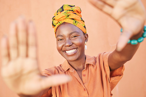 Fashion black woman, face or framing hands on orange wall background in city for profile picture, Congo branding or clothing advertising. Portrait, smile or happy model in photography pov with turban