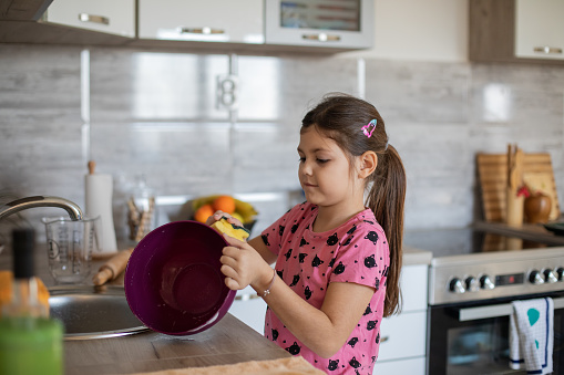 Cute little girl is washing a dishes. She likes to help her mother in the kitchen.