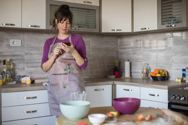 istock Young pretty woman is using her mobile phone while she is cooking 1459197740