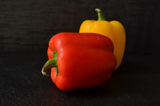 Red and yellow bell pepper is the fruit of the plants in the Grossum Group of the species Capsicum annuum. Cultivars of the plant produce fruits in different colours, including red, yellow, and green. Black background. green coloured bowl.