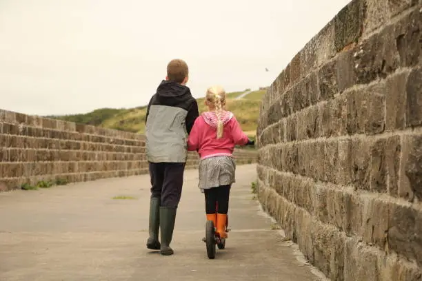 Older brother helping younger sister scoot across disused railway viaduct
