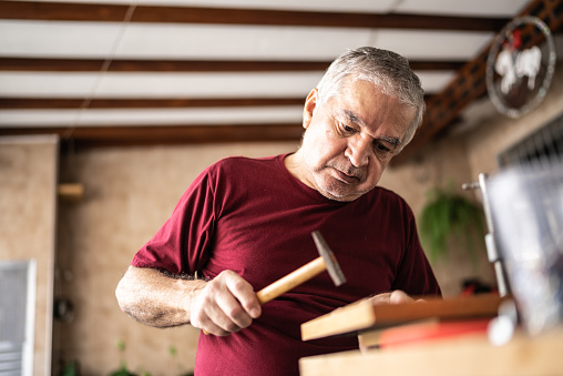 Senior man hammering a piece of wood at home