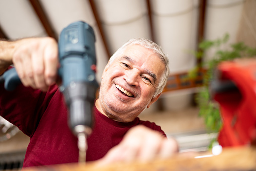 Portrait of a senior man working using a electric drill/screwdriver at home