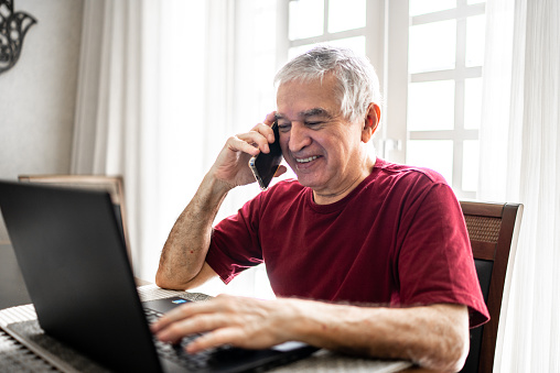 Senior man talking on the phone and using laptop at home