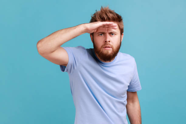 istock Man looking far away at distance with hand over head, attentively searching for bright future. 1459201034