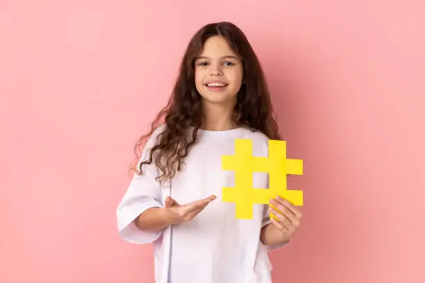 Photo of Little girl presenting big yellow hashtag symbol and smiling at camera, blogging and child content.