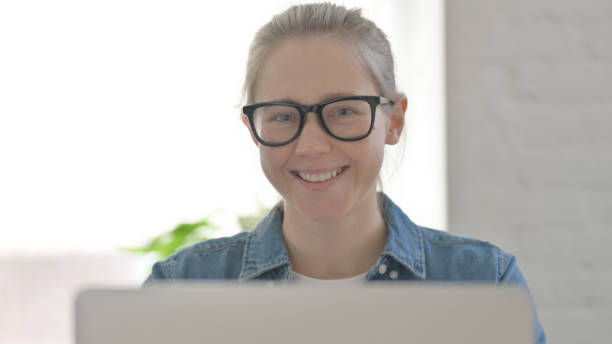istock Close up of Young Woman Smiling at Camera while using Laptop 1459201571