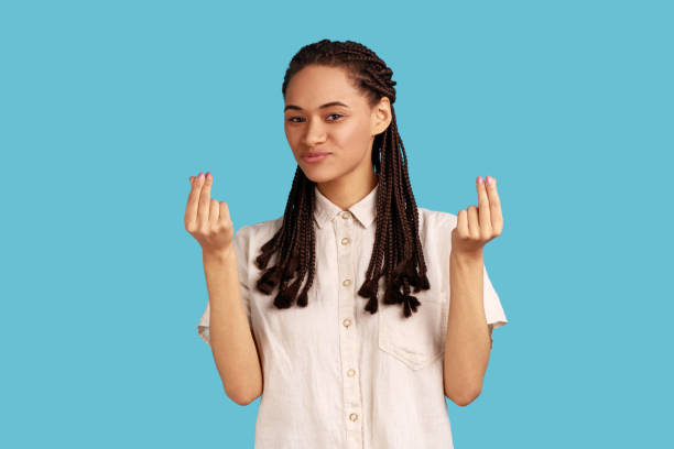 la femme avec des dreadlocks fait un geste d’argent, se frotte les doigts, regarde la caméra avec une expression heureuse. - women currency white savings photos et images de collection