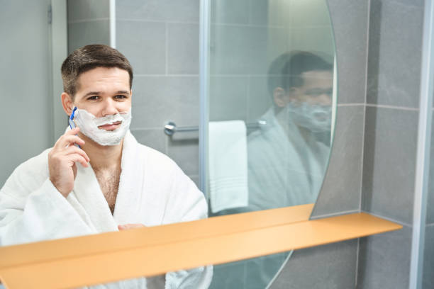 istock Young guy in a bathrobe shaves his cheek with razor 1459211821