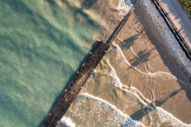 Beautiful top down shot of the shoreline of Lake Michigan with a concrete pier and breakwater diagonally across the frame with sunshine lighting up the sandy shoreline and turquoise waters. stock photo